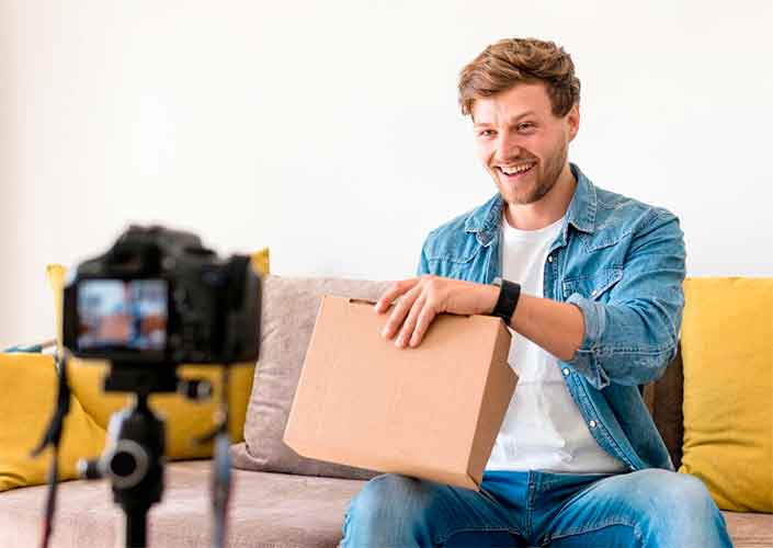 Foto de homem abrindo caixa de produto na frente de uma câmera para transmitir a ideia de unboxing e de produção de conteúdo