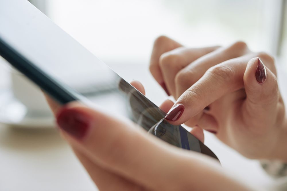 app commerce Mãos com unhas pintadas de vermelho manuseando um tablet com os dedos, simbolizando a experiência de compra em app commerce.