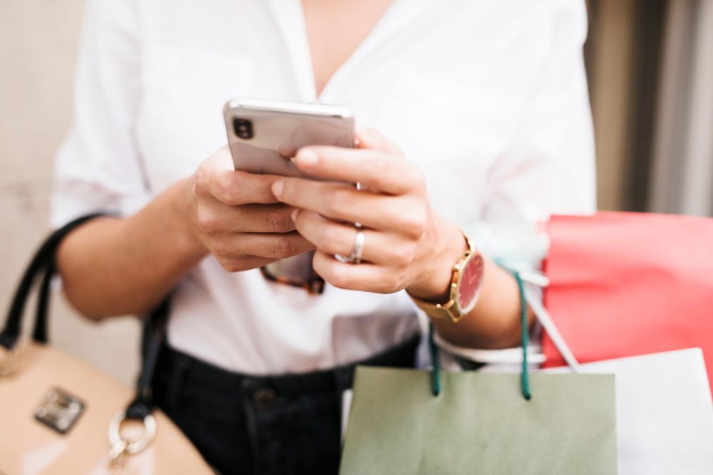 mobile first Close das mãos de uma mulher segurando um smartphone e sacolas de compras, ilustrando a experiência do consumidor mobile first.