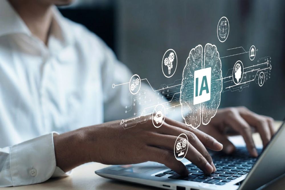 agentes de IA Um homem em camisa social branca digitando em um notebook prateado em uma mesa de escritório. Flutuando à frente dele, há uma sobreposição gráfica vibrante de um cérebro cibernético feito de circuitos com "IA" escrito no centro. Ícones conectados por linhas de dados, representando conceitos de inteligência artificial, como chatbots e engrenagens, ilustram a interação e o controle de agentes de ia na automação de tarefas empresariais.