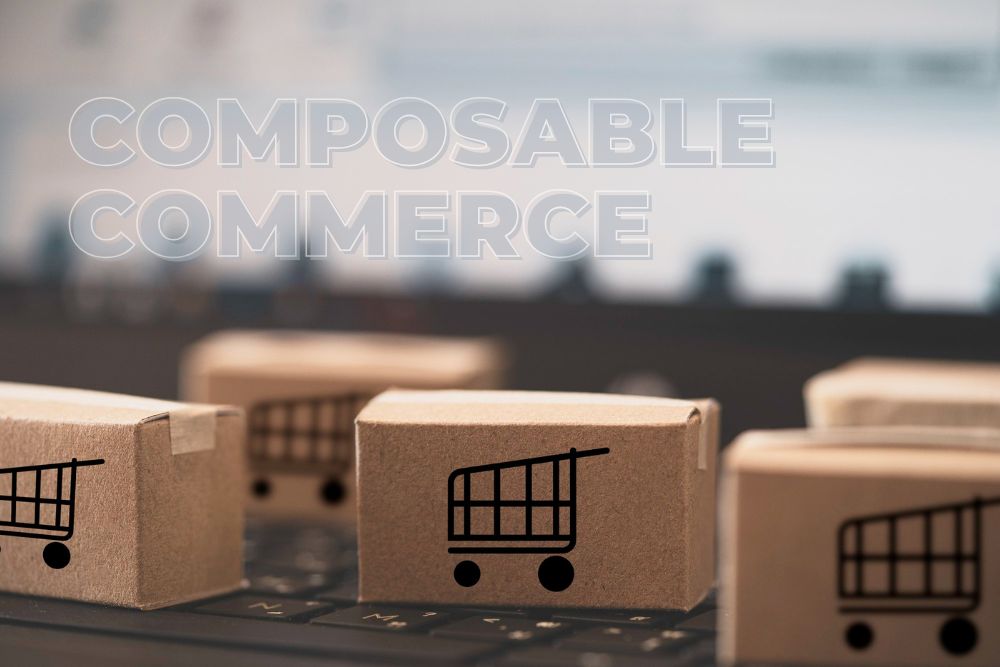 composable commerce Uma imagem conceitual ilustrando o composable commerce. Várias pequenas caixas de papelão marrom, cada uma com um ícone de carrinho de compras preto impresso, estão dispostas sobre o teclado desfocado de um laptop. O texto translúcido e contornado 'COMPOSABLE COMMERCE' está sobreposto no topo da imagem, simbolizando a modularidade e a flexibilidade das operações de e-commerce moderno